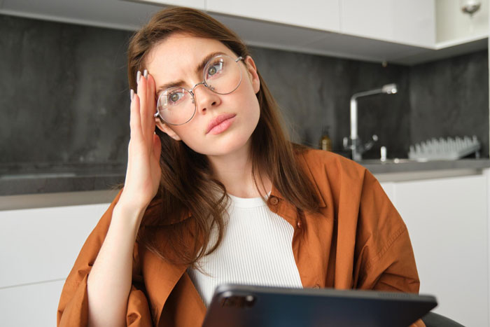 Young woman wearing glasses looks stressed and confused while holding a tablet, reacting to charges for raising her as a minor. Young woman wearing glasses looks stressed and confused while holding a tablet, reacting to charges for raising her as a minor.