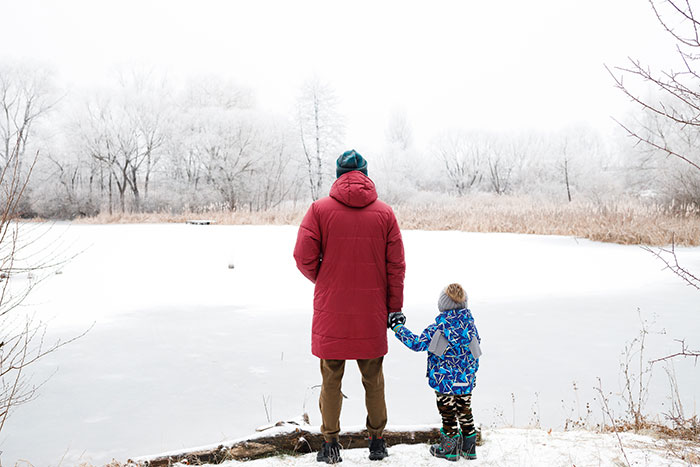 Man in red coat holding child&rsquo;s hand by frozen lake in winter, illustrating selfish dad demands apology from daughter story.