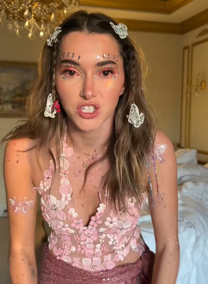 Young female influencer with butterfly accessories and glitter on face and arms, criticized for partying with contagious infection. Young female influencer with butterfly accessories and glitter on face and arms, criticized for partying with contagious infection.
