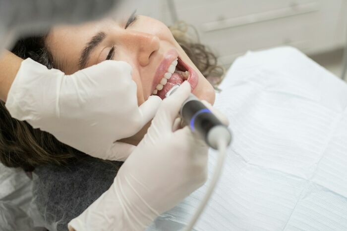 Dentist wearing gloves performing a dental cleaning on a female patient in a clinical setting.
