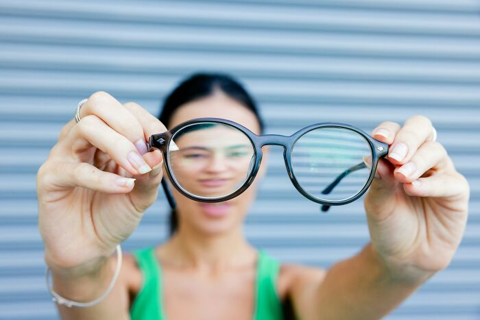 Woman holding glasses showing clear lenses symbolizing internet users debunking common scams that aren’t really scams