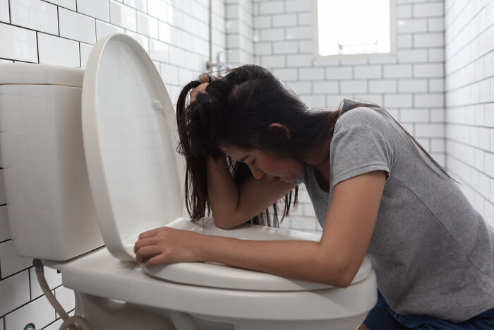 Woman feeling nauseous and sick leaning over a toilet in a bathroom, reflecting on wildest patient horror stories dentists share.
