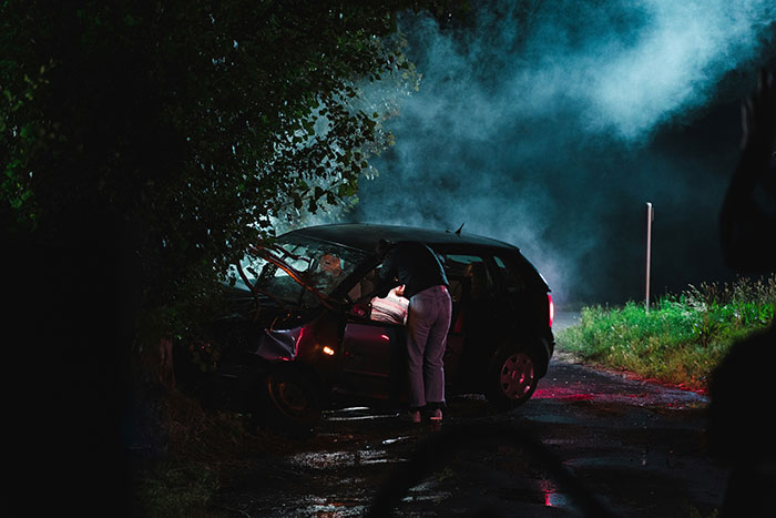 Woman trusting intuition after car crash at night on a dark rural road with smoke rising nearby