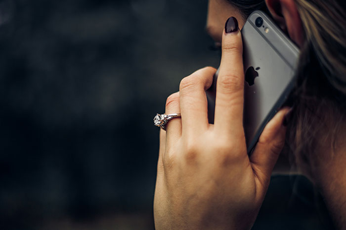 Woman with engagement ring holding iPhone to ear, illustrating women sharing times intuition was spot on.