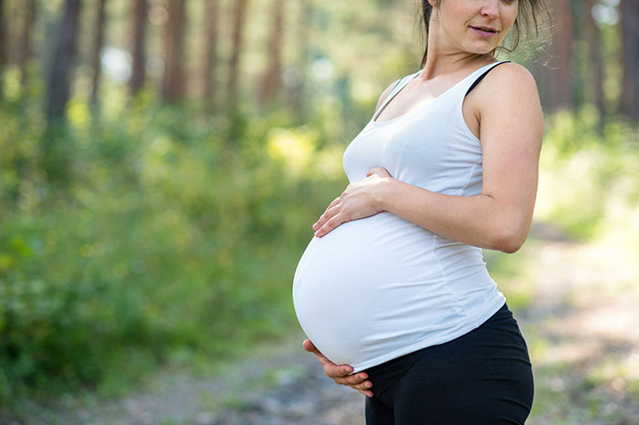 Pregnant woman outdoors in a white tank top, illustrating women's intuition and experiences with strong gut feelings.