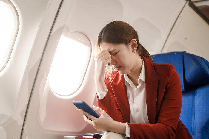 Passenger on airplane in red jacket looking distressed while holding phone near window, illustrating flight crew horror stories.
