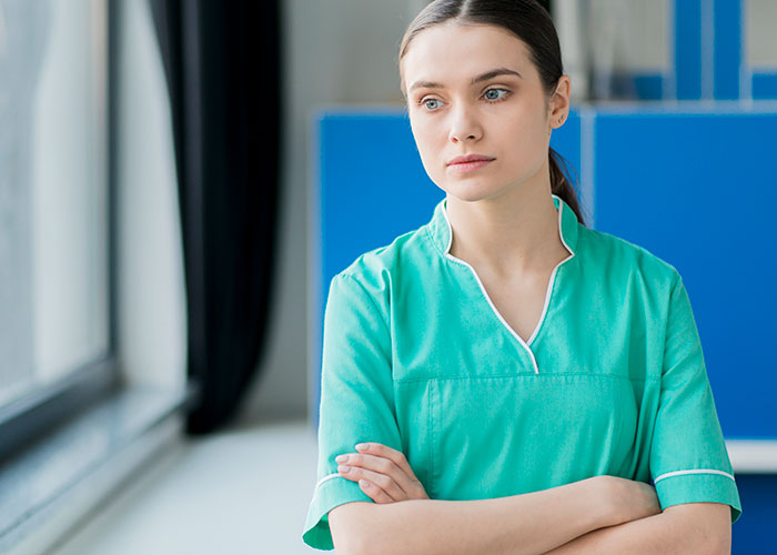 Female hospital employee in green scrubs looking concerned, illustrating impact of family first vacation policy issues.