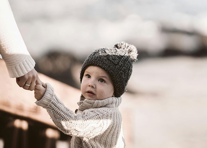 Toddler wearing knit hat and sweater holding adult&rsquo;s hand, illustrating hospital family first vacation policy impact.