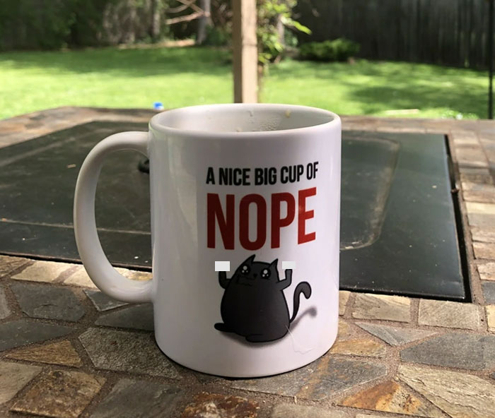 White mug with a cartoon cat and text on a patio table, reflecting a friend who doesn't understand clingy children on vacation.