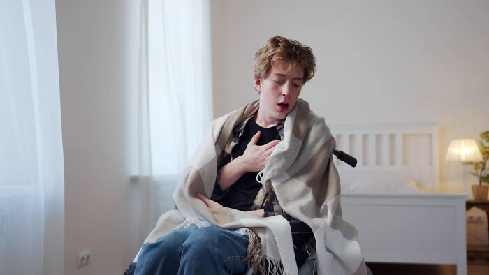 Young man clutching chest in a wheelchair, wrapped in a blanket, depicting heart racing in a medical context.