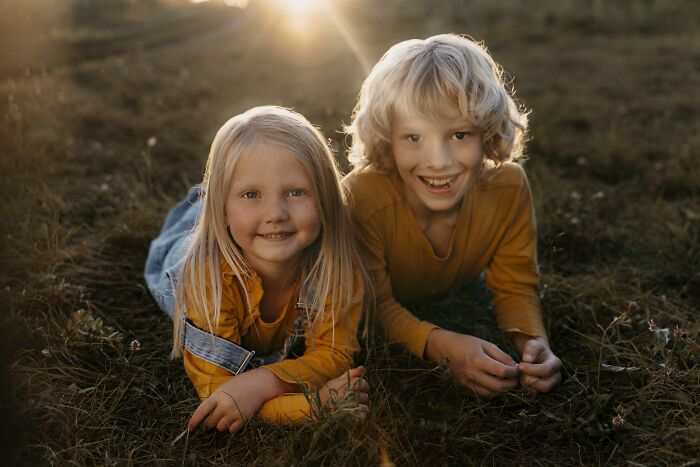 Two children lying on grass at sunset, capturing the contrast of joyful moments with the theme of regret having kids.