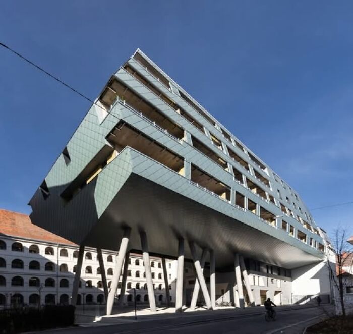Unesthetic modern architecture building with an unusual cantilever design supported by angled columns under a clear blue sky.