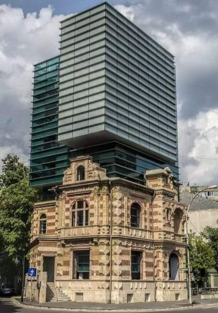 Modern architecture building with an unesthetic glass extension above an old, ornate historic structure under a cloudy sky