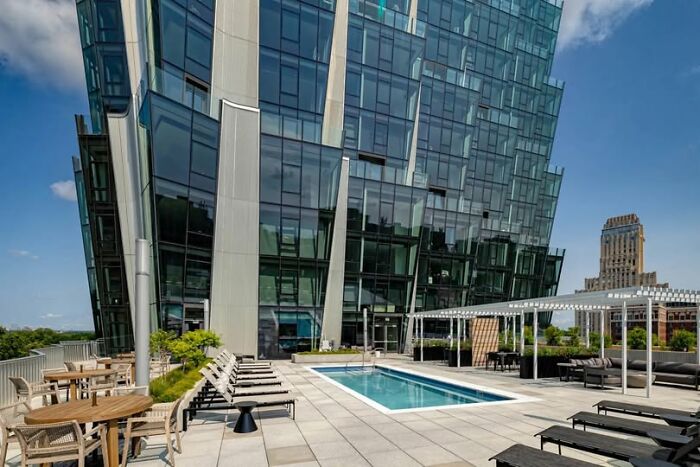 Modern architecture featuring a glass building with an outdoor pool and seating area in an urban setting.