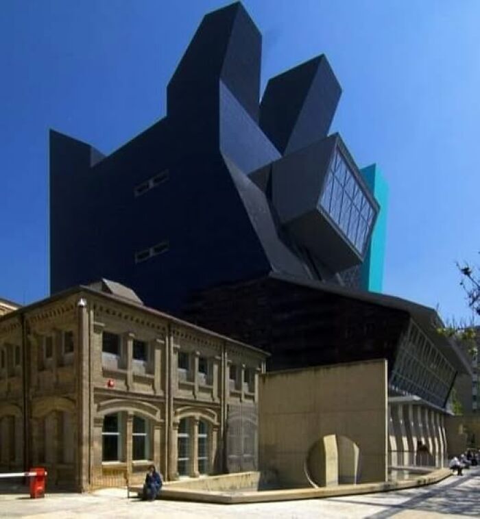 Modern architecture featuring an ugly, unesthetic building with sharp, irregular shapes contrasting an older structure.