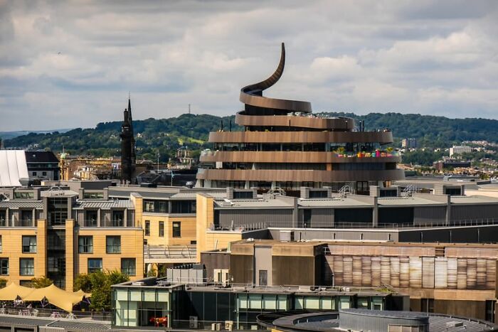 Spiral-shaped modern building among other urban structures, showcasing unusual and unesthetic architecture design.