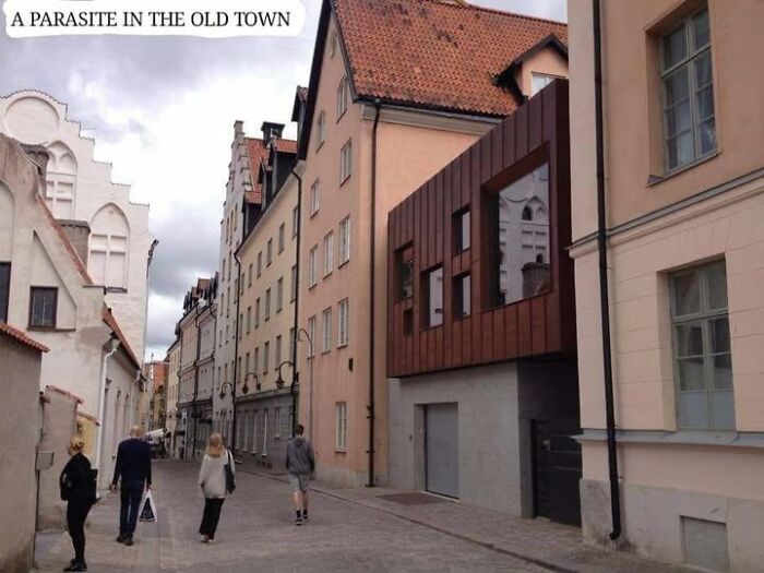 A modern, unesthetic building contrasting with old town architecture on a pedestrian street with passersby.