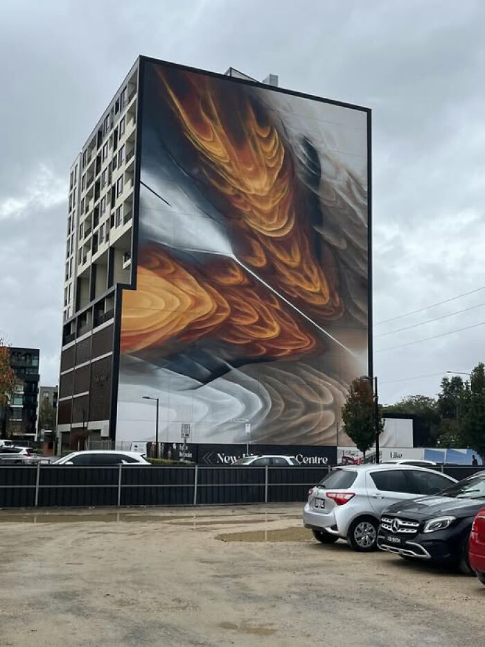 Tall building with abstract mural and parked cars in front, example of ugly unesthetic buildings in modern architecture.