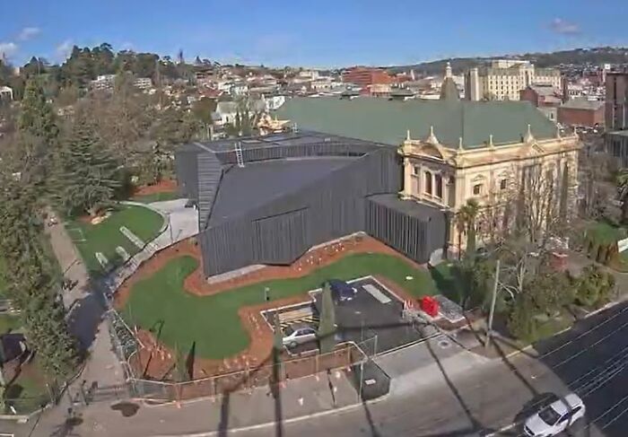 A large unesthetic and ugly modern building next to a classical architectural structure in an urban area.