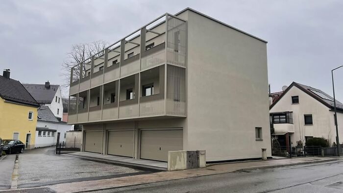 Minimalist gray building with balconies and garages in a residential area, example of ugly unesthetic modern architecture.