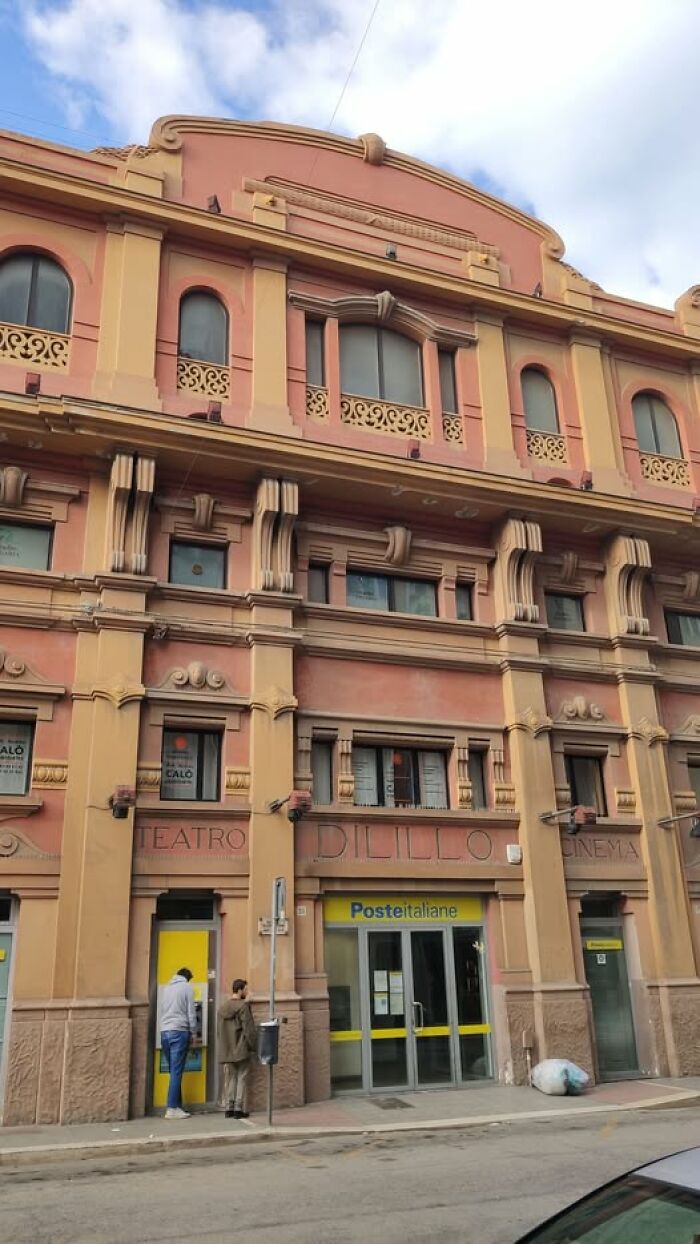 Unesthetic building facade with ornate detailing and faded paint, housing a postal office and featuring old architectural elements.