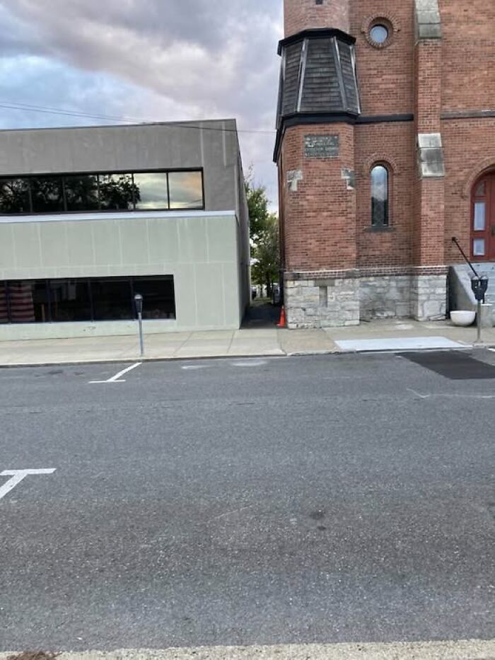 Modern architecture showing a stark contrast between a plain gray building and an old brick structure on a quiet street.