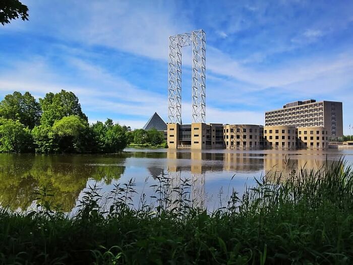 Unesthetic modern architecture featuring an unusual building with a geometric metal frame and concrete structures by a lake.