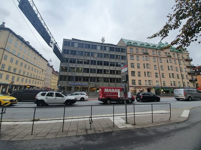Ugly and unesthetic modern architecture building in a city street with multiple cars and cloudy sky.
