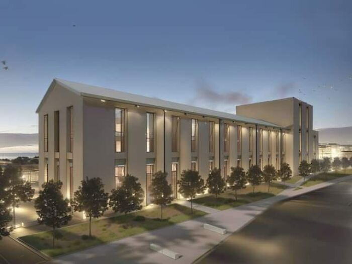 Modern architecture building at dusk with unesthetic design, illuminated windows, and trees along the sidewalk.