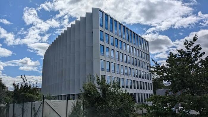Modern architecture example of an ugly and unesthetic building with gray facade and reflective windows under a cloudy sky.