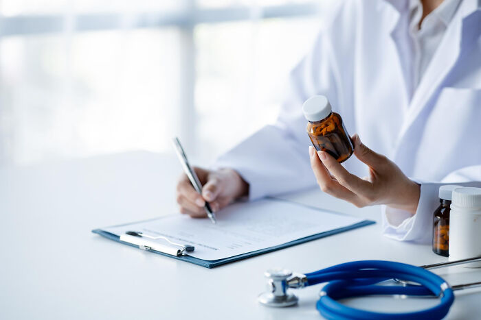 Person in a white coat holding a medicine bottle and writing notes, highlighting upcoming events from an online thread.
