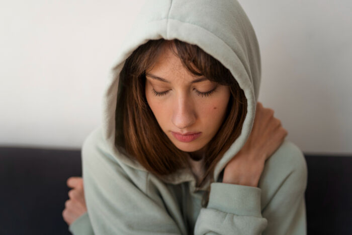 Young woman wearing a hoodie, looking down and reflecting, illustrating focus on upcoming events shared in an online thread.