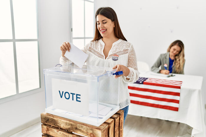 Woman casting ballot in clear box at voting event, highlighting key upcoming events shared in an online thread.
