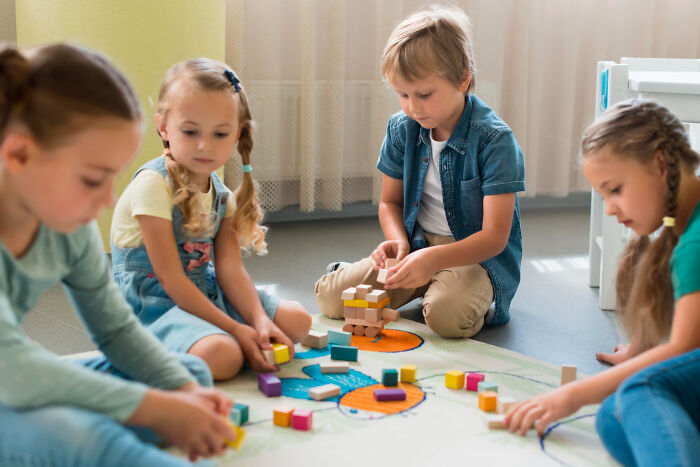 Four children playing with colorful blocks on the floor, illustrating upcoming events shared online thread insights.