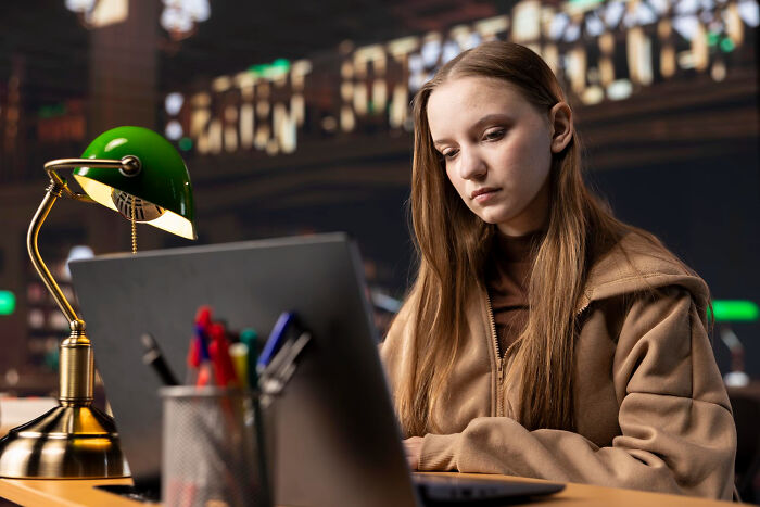 Young woman focused on laptop in a cozy setting, reading an online thread about upcoming events to watch closely.