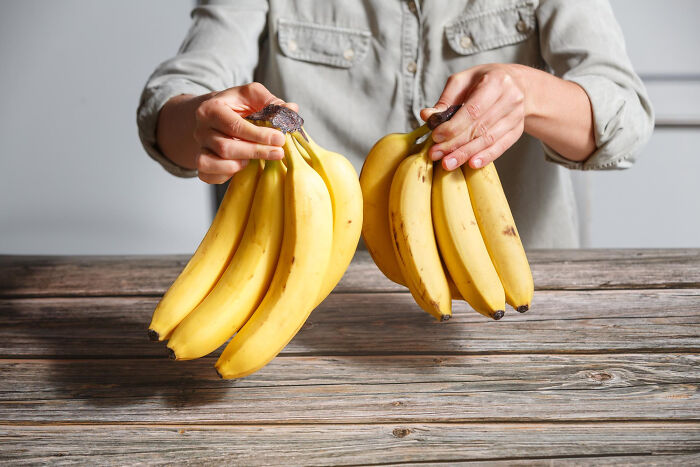 Person holding two bunches of ripe bananas over a wooden table, illustrating key online thread events concept.