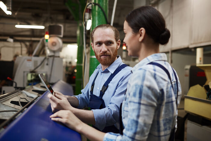 Two factory workers discussing upcoming events on a tablet, highlighting important online thread updates.