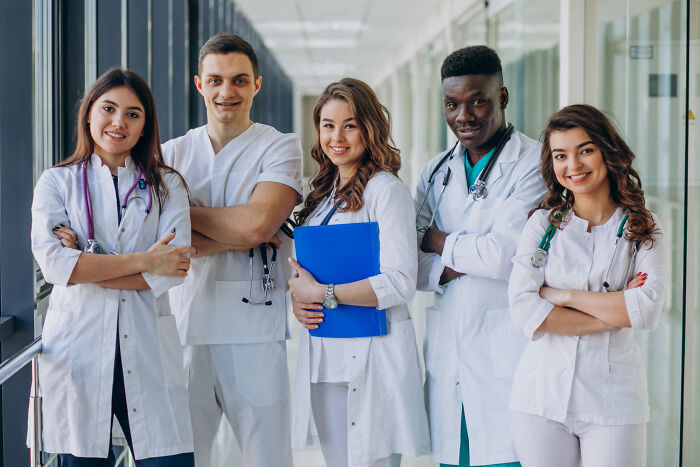 Group of diverse medical professionals standing in hospital corridor, highlighting online thread sharing upcoming events to watch.