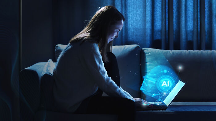 Woman sitting on a couch at night using a laptop with AI hologram effects representing an online thread sharing upcoming events.