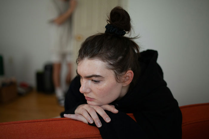 Sad teen with hair in a bun leans on couch, showing refusal and distress related to special needs stepsister hospital visit.