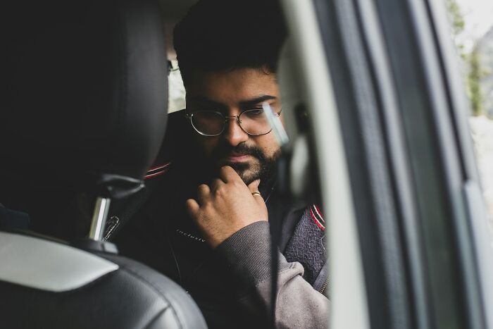 Man with glasses and beard sitting in a car, deep in thought, relating to funny steak and lobster complaints.