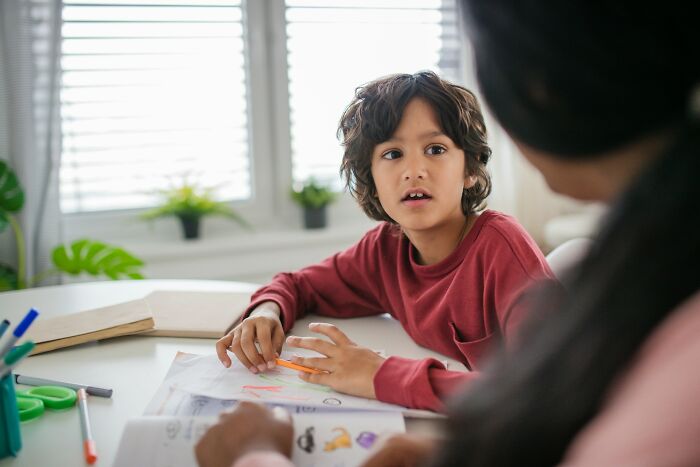 Young boy in red shirt discussing a family story about the golden child with an adult at a table.