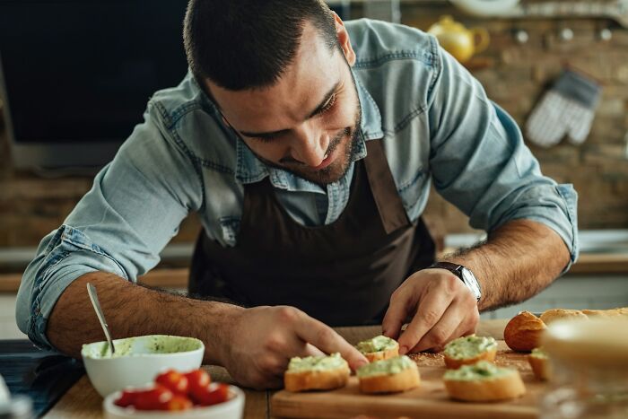 Man wearing apron carefully preparing small appetizers in kitchen, emphasizing the importance of sharpen your knives.