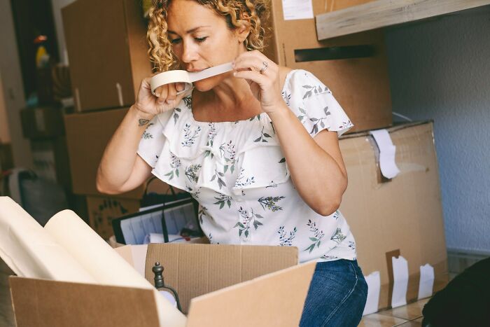 Woman packing boxes in a cluttered room, appearing focused and stressed, symbolizing uniquely awkward wedding mishaps.