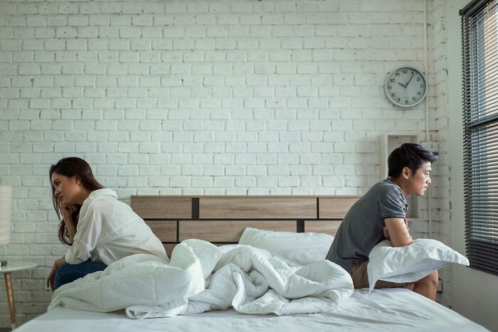 A couple sitting apart on a bed in a bedroom, illustrating family tension and challenges with the golden child concept.