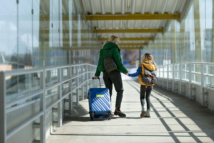 Mother and child holding hands walking with luggage in a glass corridor illustrating funny moments with loved ones.