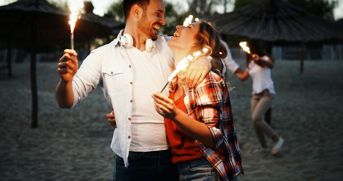 Couple smiling and holding sparklers on a beach at dusk, illustrating toxic relationship traits and emotional dynamics.