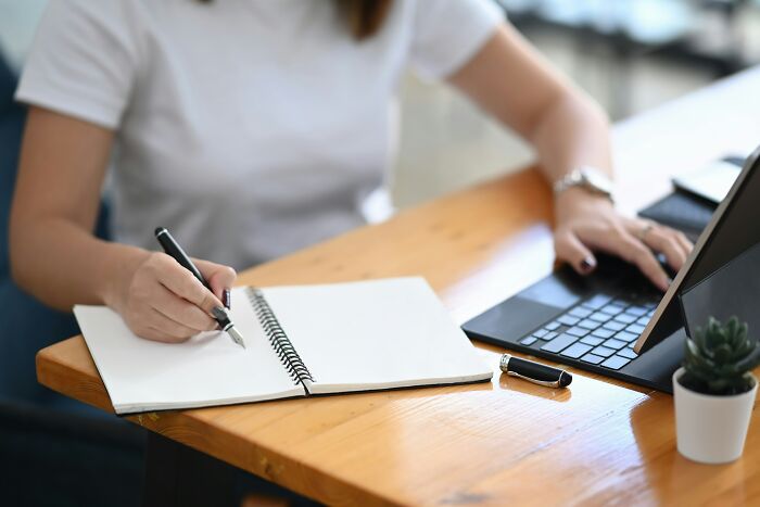 Person working at a wooden desk with a notebook and laptop illustrating common work experiences with we’ve always done it this way mindset