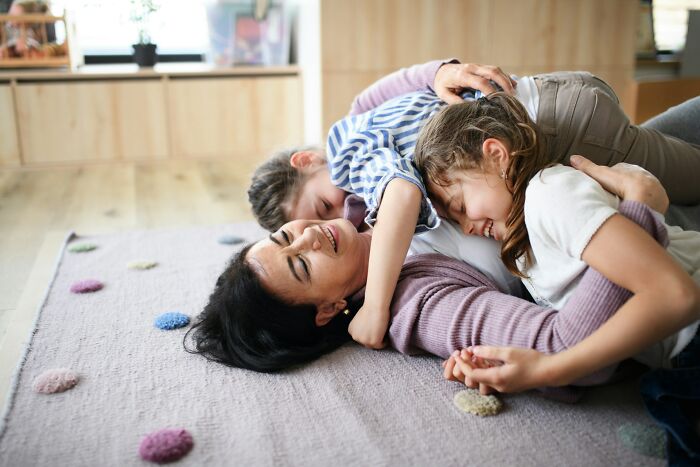 Mother and children playing on the floor, illustrating family dynamics and golden child challenges in a warm home setting.