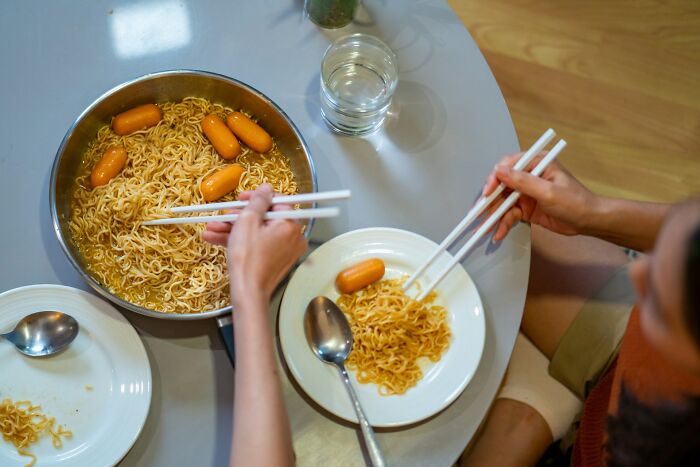 Two people using chopsticks to eat noodles and sausages, illustrating surprising habits discovered after moving in with partner.